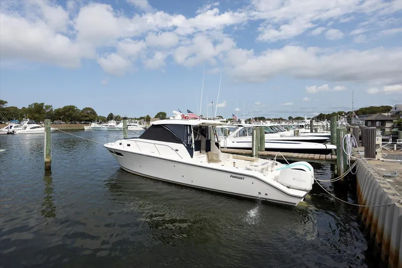 Slide: The Image of 2016 Pursuit OS 355 Offshore boat docked in a marina under a partly cloudy sky. - 0