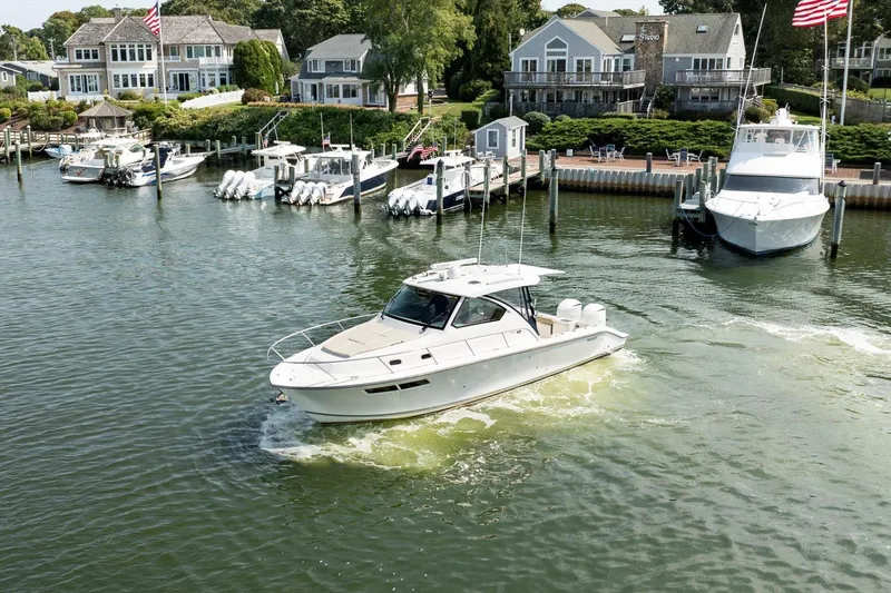 Slide: The Image of 2016 Pursuit OS 355 Offshore boat cruising in a scenic marina with waterfront homes. - 3