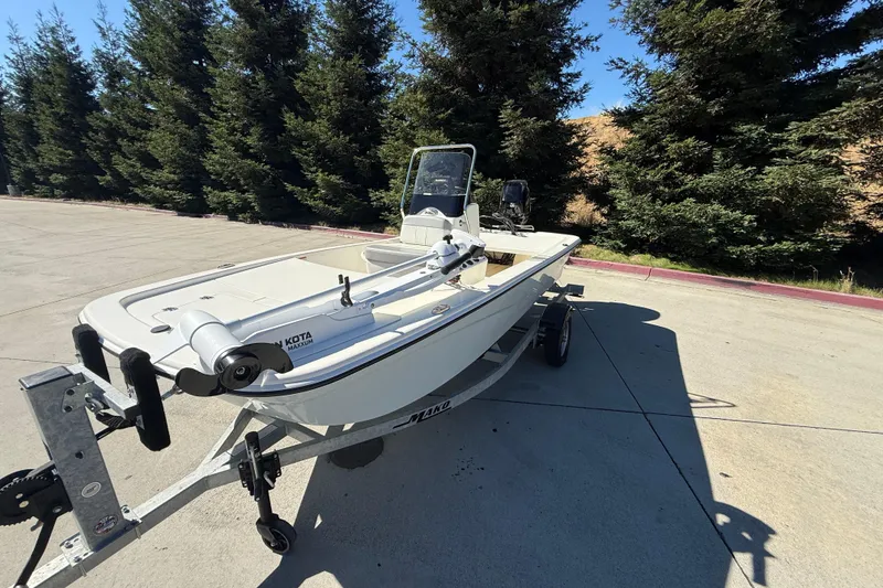 Slide: The Image of 2024 Mako Pro Skiff 13 CC boat on trailer, parked outdoors near trees. - 2