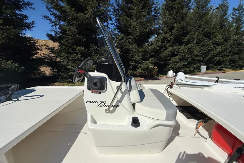 Slide: The Image of 2024 Mako Pro Skiff 13 CC boat with steering console, set against a backdrop of trees. - 5