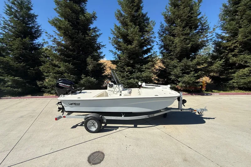 Slide: The Image of 2024 Mako Pro Skiff 13 CC boat on trailer, parked outdoors with trees in background. - 59