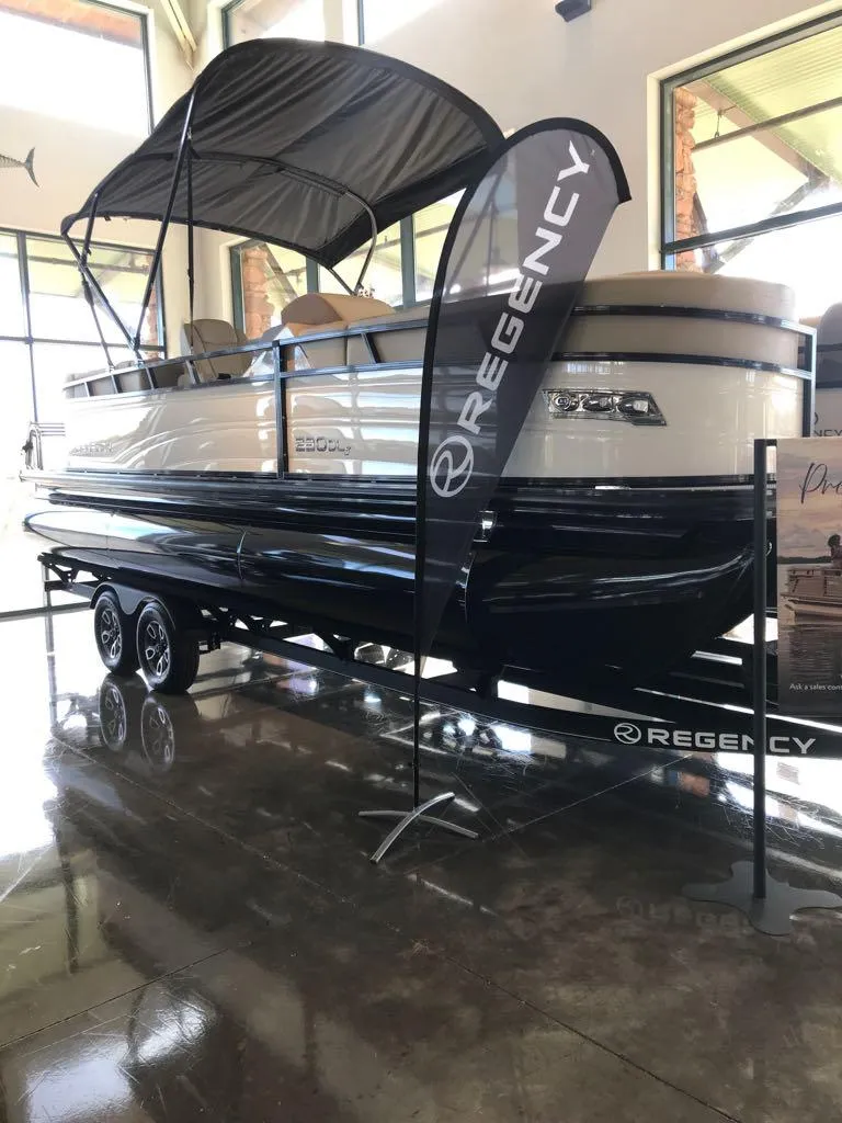 Slide: The Image of 2024 Regency 230 DL3 pontoon boat displayed indoors with canopy and branding. - 2