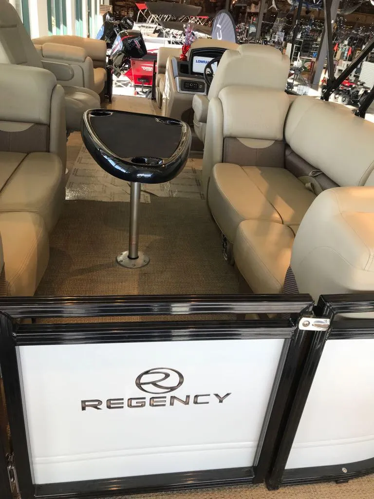 Slide: The Image of 2024 Regency 230 DL3 pontoon boat interior with beige seating and sleek table. - 4