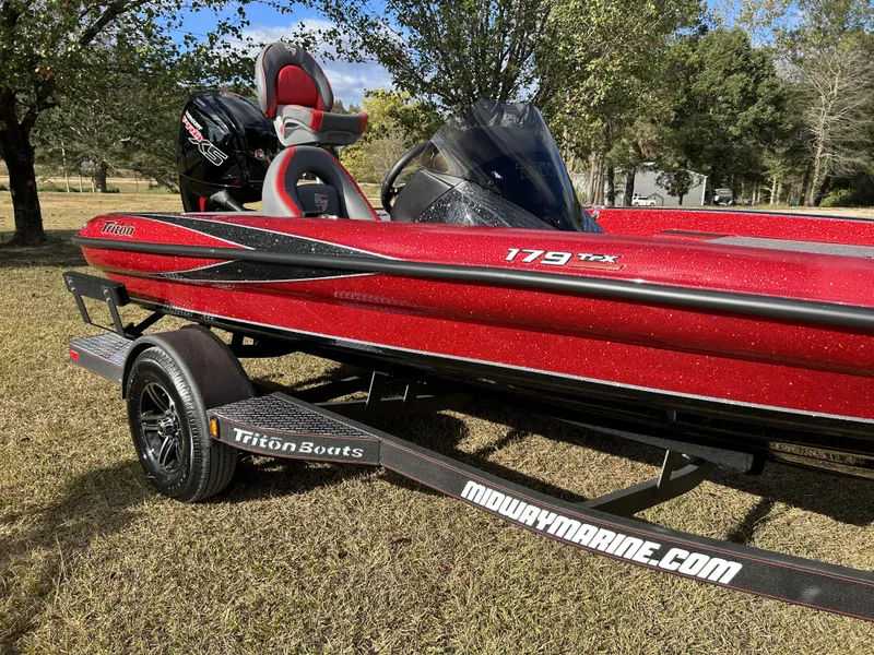 Slide: The Image of 2024 Triton 179 TrX red bass boat on trailer in grassy area. - 9