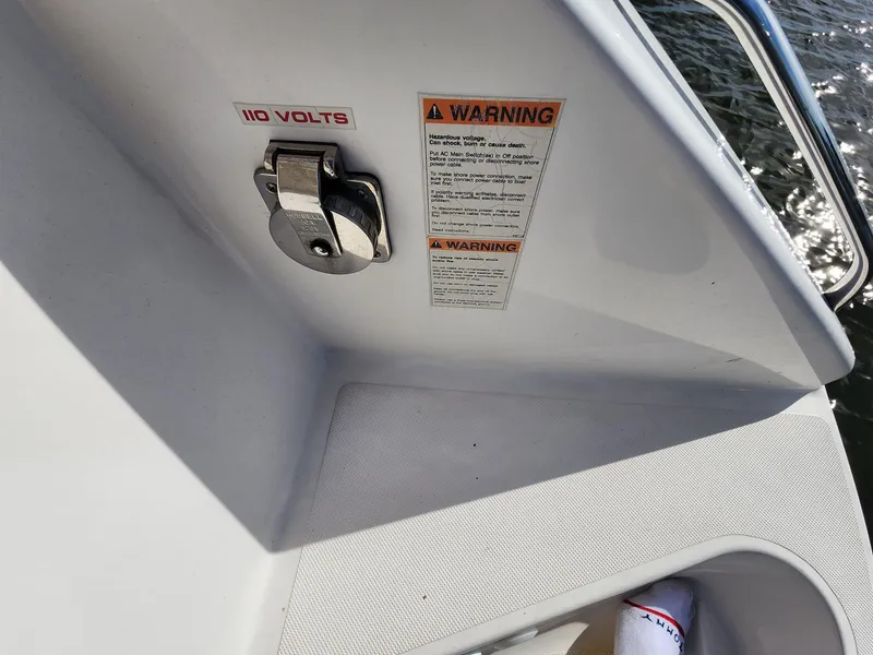 Slide: The Image of 110-volt outlet and warning labels on 2017 Pursuit S 280 Sport boat. - 35