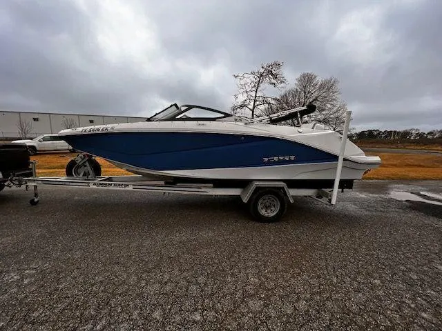 Slide: The Image of 2014 Scarab 215 boat on a trailer, blue and white, parked outdoors. - 2