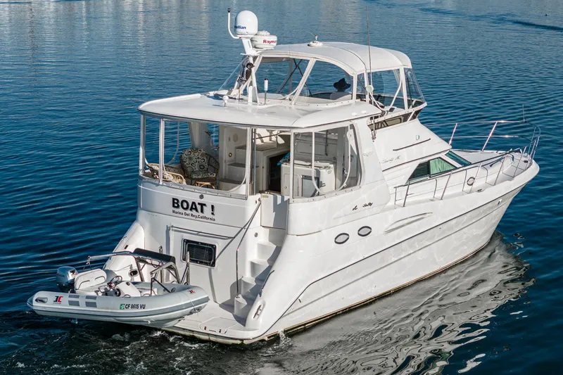 Slide: The Image of 1997 Sea Ray 420 Aft Cabin yacht cruising on water with a small dinghy attached. - 13