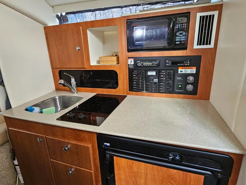 Slide: The Image of 2006 Bayliner 325 boat kitchen with sink, stove, microwave, and storage cabinets. - 7