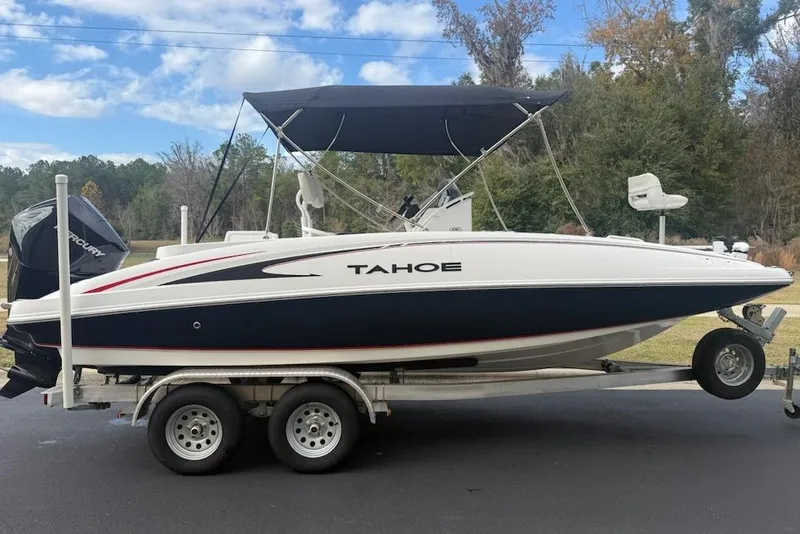 The Image of 2023 Tahoe 2150 boat on trailer with canopy, parked outdoors under blue sky. - 0