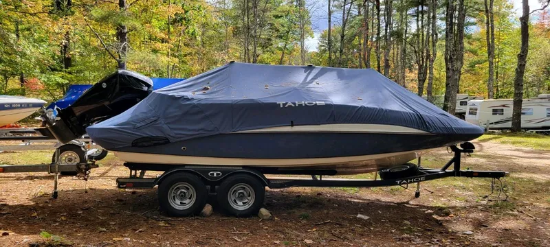 Slide: The Image of 2022 Tahoe 2150 boat covered on a trailer in a wooded area. - 4