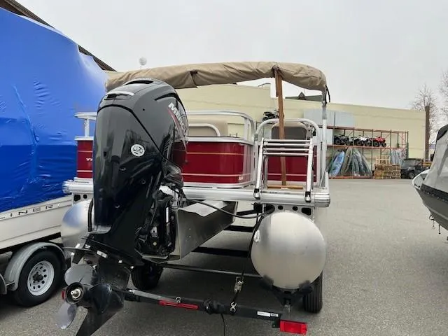 Slide: The Image of 2024 Sun Tracker Bass Buggy 18 DLX pontoon boat with outboard motor in a storage area. - 2