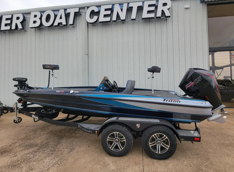 Slide: The Image of 2024 Triton 19 TrX bass boat on trailer outside a boat center. - 1