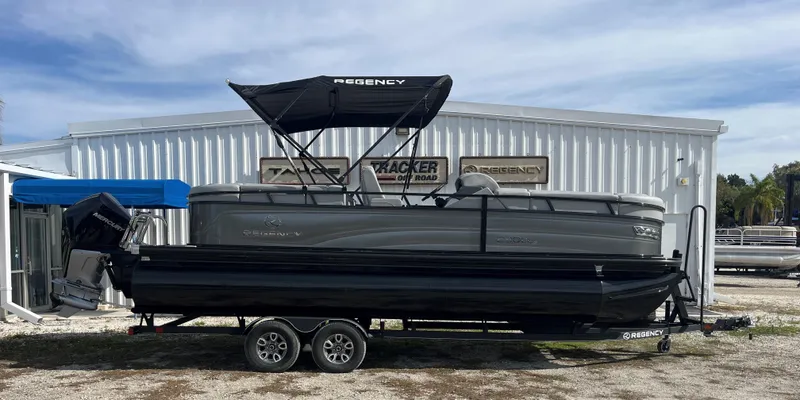 The Image of 2024 Regency 230 DL3 pontoon boat on trailer, parked outside dealership. - 0