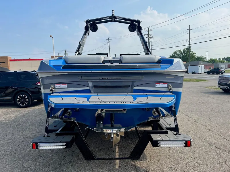 Slide: The Image of 2024 Centurion Ri245 boat, rear view, blue and gray, parked on a trailer. - 2