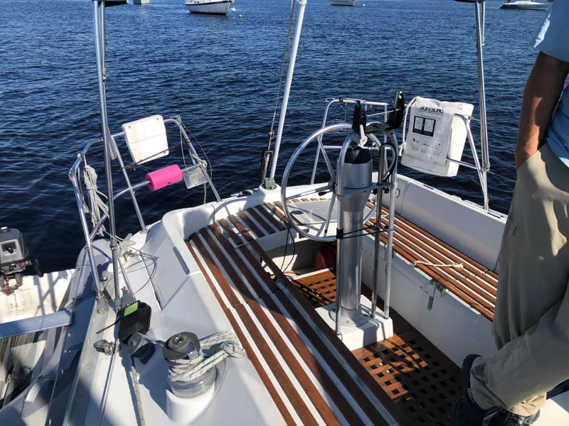 Slide: The Image of 1985 Beneteau First 345 sailboat cockpit with wooden deck and steering wheel, moored on calm water. - 41