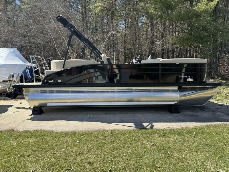 Slide: The Image of 2024 Harris Cruiser 210 pontoon boat on a concrete surface with trees in the background. - 1