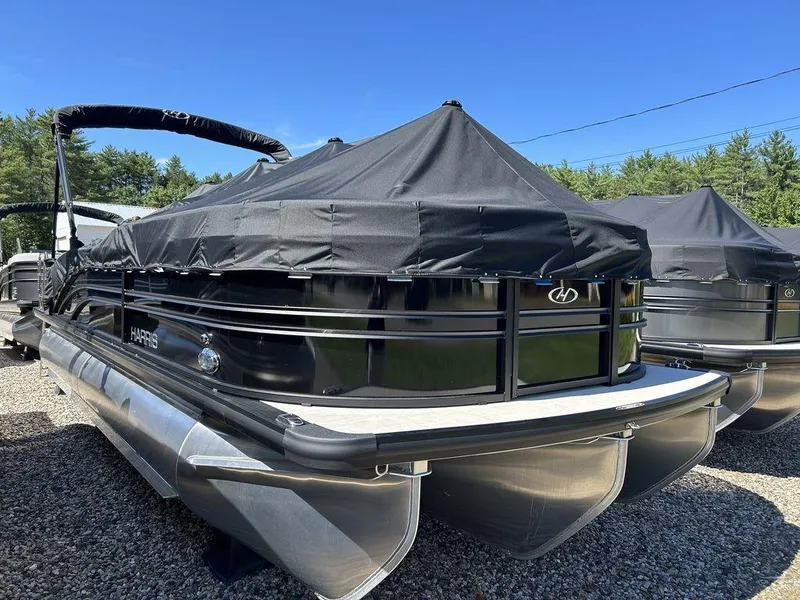 Slide: The Image of 2024 Harris Sunliner 230 pontoon boat with black cover, parked outdoors. - 3
