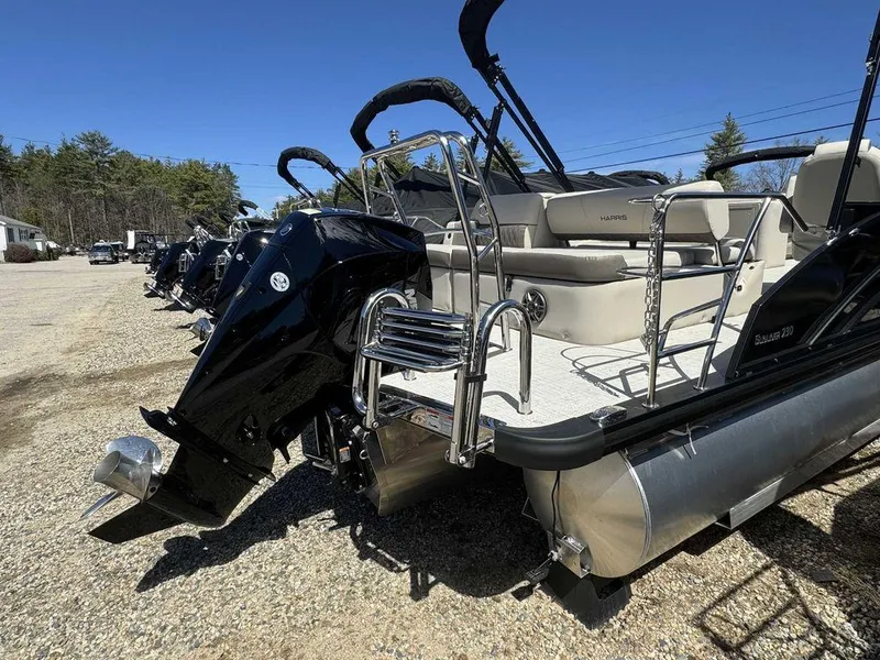 Slide: The Image of 2024 Harris Sunliner 230 pontoon boat with outboard motor, parked on gravel lot. - 9