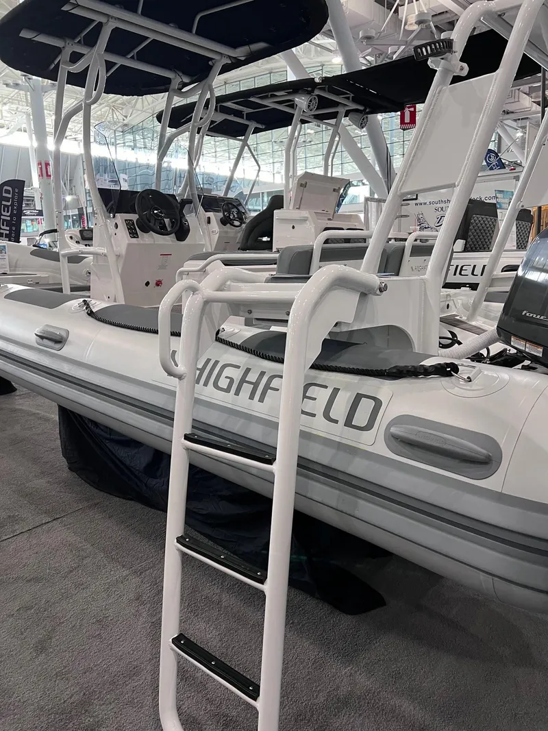 Slide: The Image of 2024 Highfield Patrol 600 inflatable boat with ladder and canopy at a boat show. - 11