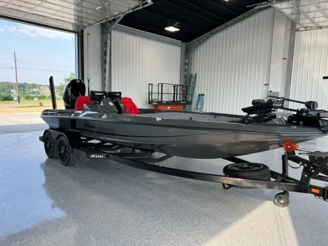 Slide: The Image of 2024 iKon LX21 boat in a garage, black exterior, red seats, on a trailer. - 2