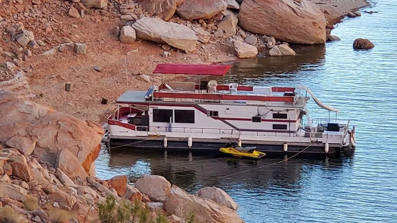 Slide: The Image of 1978 Kayot houseboat docked by rocky shoreline with a yellow kayak nearby. - 3