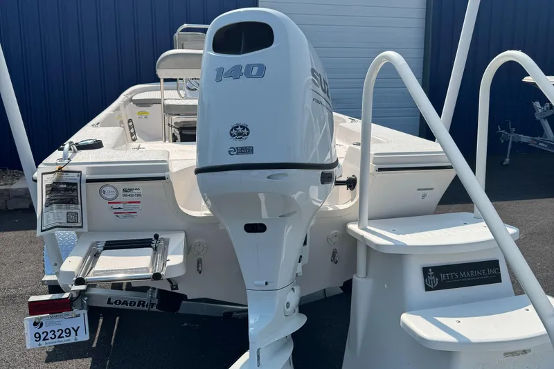 Slide: The Image of 2025 Carolina Skiff 192 JLS boat with Suzuki 140 outboard motor, parked near blue building. - 4
