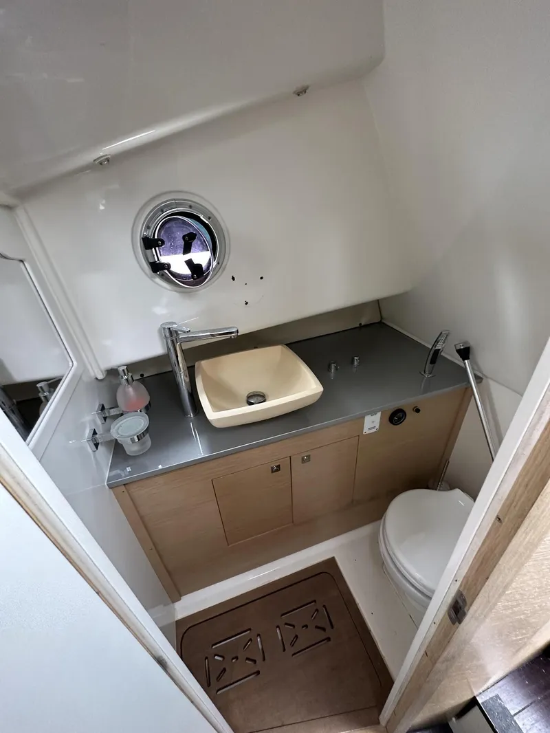 Slide: The Image of 2014 SACS Strider 13 boat bathroom with sink, toilet, and porthole window. - 25