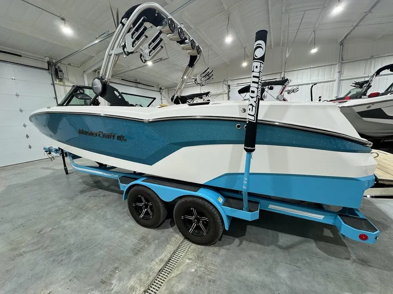 Slide: The Image of 2022 MasterCraft NXT24 boat on a blue trailer in a showroom. - 0
