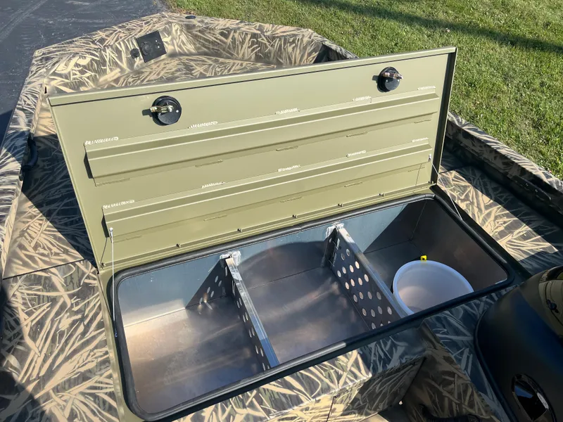 Slide: The Image of 2024 Lowe Outlet 20 boat storage compartment with open lid, showcasing interior dividers and camo design. - 12