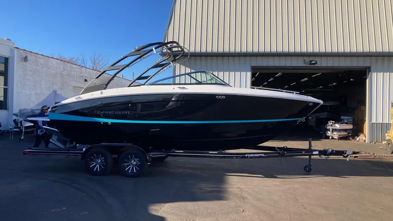 Slide: The Image of 2024 Regal LS4 Surf boat on trailer outside a warehouse. - 0