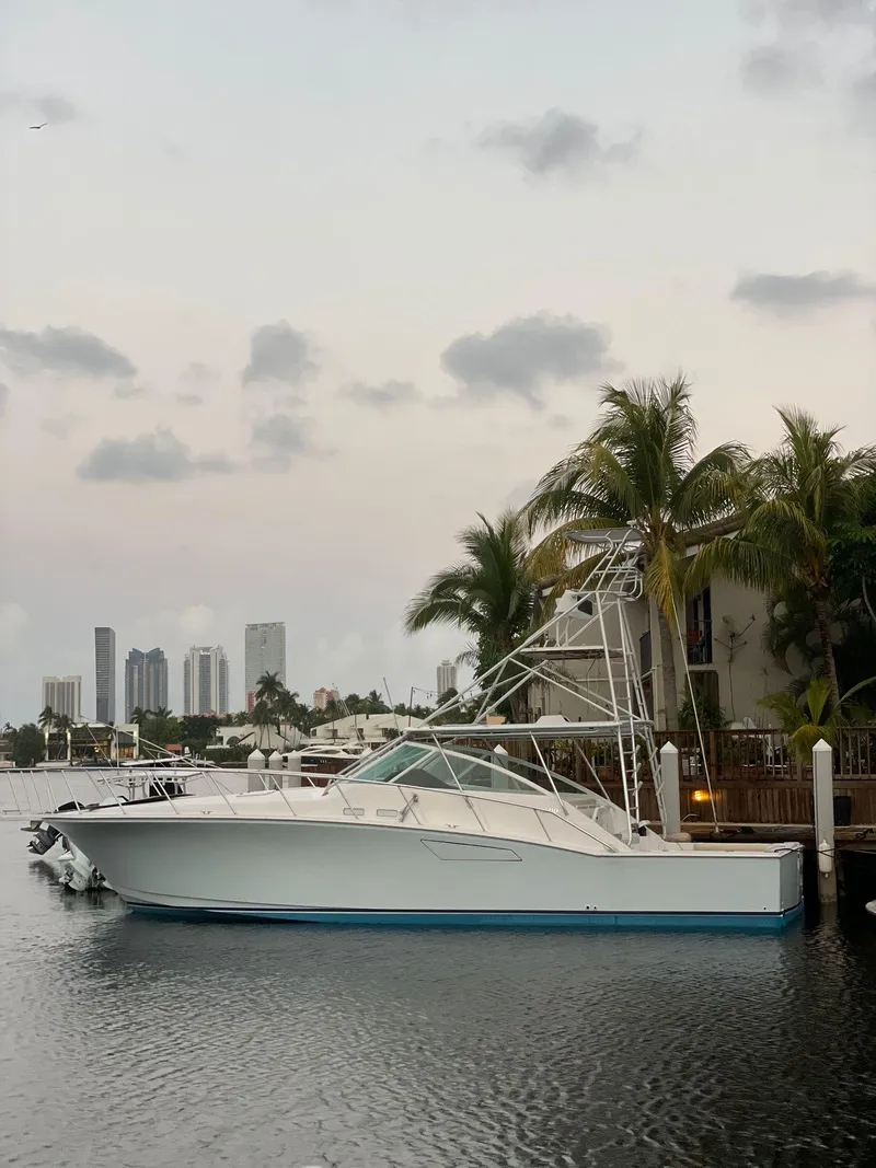 Slide: The Image of 2003 Cabo 45 Express boat docked near palm trees with city skyline in the background. - 2