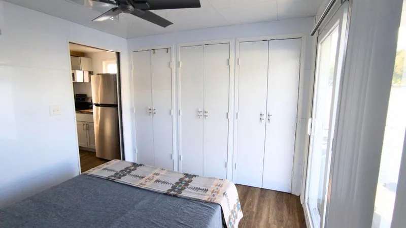 Slide: The Image of Modern 2022 houseboat bedroom with closet, ceiling fan, and kitchen view. - 11
