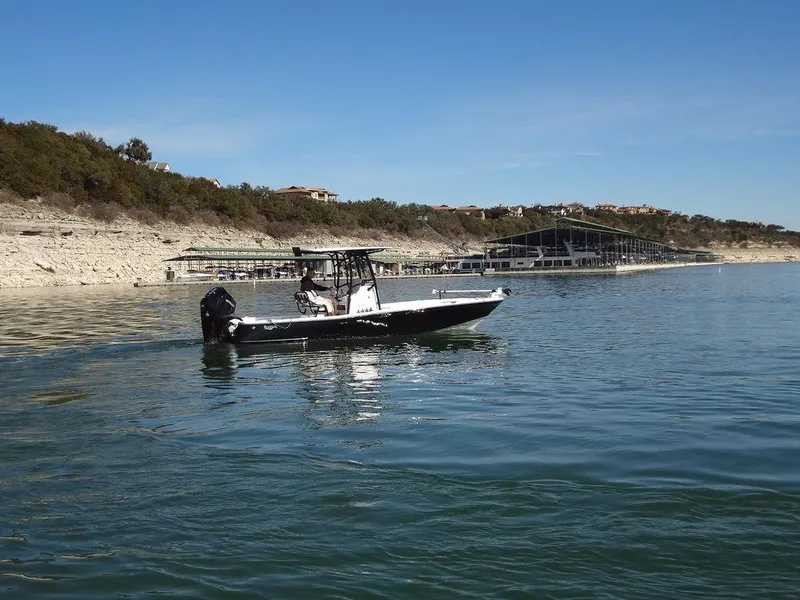 Slide: The Image of 2024 BlackJack 256 Bay boat cruising on a calm lake near a marina. - 11