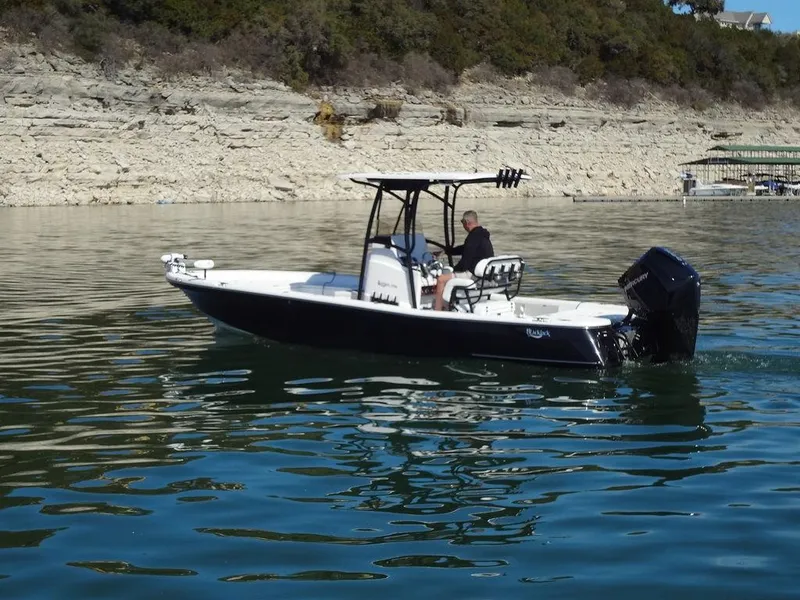 Slide: The Image of 2024 BlackJack 256 Bay boat cruising on a calm lake near rocky shoreline. - 34
