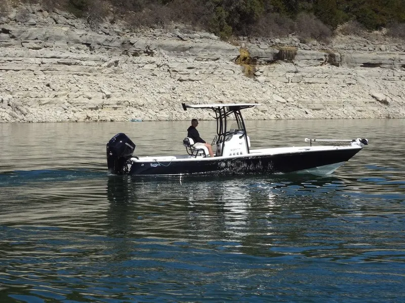 Slide: The Image of 2024 BlackJack 256 Bay boat cruising on a calm lake near rocky shoreline. - 4