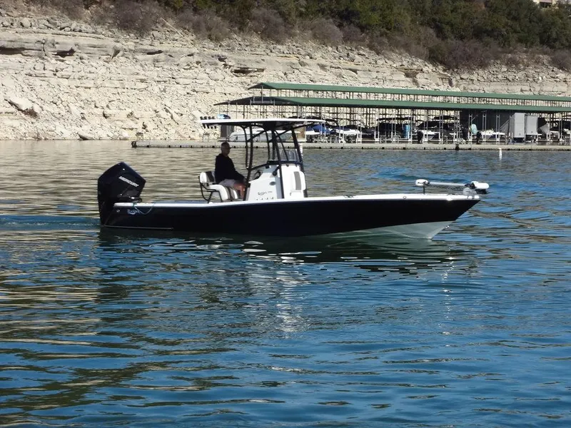 Slide: The Image of 2024 BlackJack 256 Bay boat cruising on a calm lake near a rocky shoreline. - 6