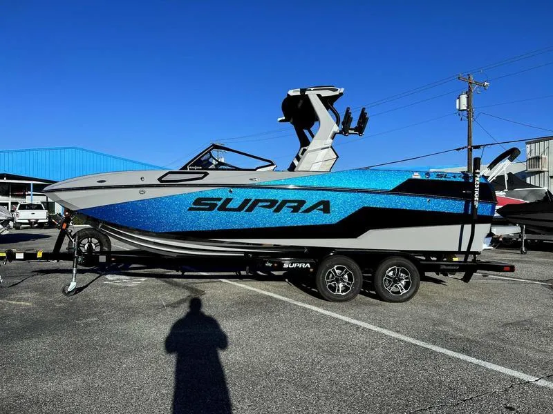 Slide: The Image of 2024 Supra SL boat with blue and black design on a trailer in a parking lot. - 10