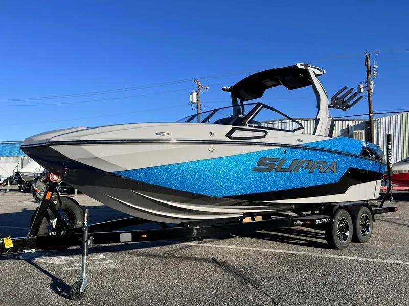 Slide: The Image of 2024 Supra SL boat with blue accents on a trailer, parked outdoors. - 3