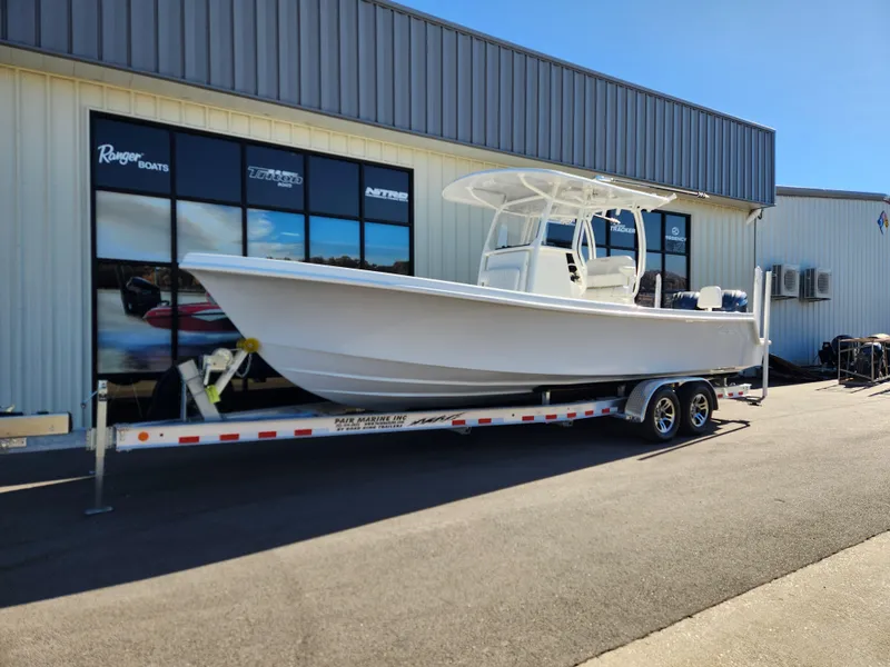 Slide: The Image of 2024 Pair Customs 27 CC boat on trailer, parked outdoors, surrounded by trees. - 1