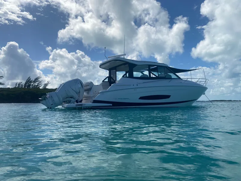 Slide: The Image of 2023 Regal 36 XO boat anchored in clear blue water under a partly cloudy sky. - 2