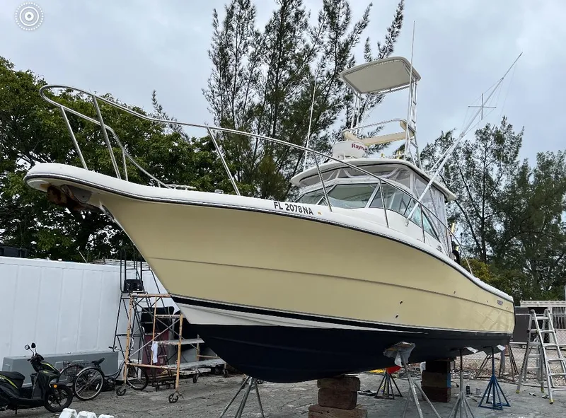 Slide: The Image of 2005 Pursuit 3070 Offshore boat on dry dock, surrounded by trees and equipment. - 2
