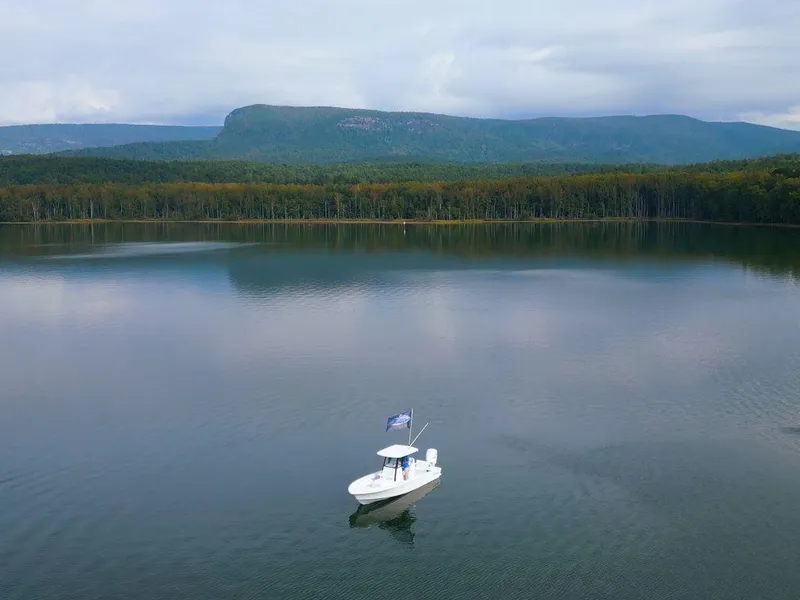 Slide: The Image of 2024 Sportsman Masters 267OE Bay boat on serene lake with mountain backdrop. - 10