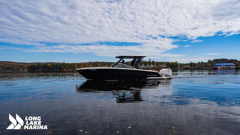 Slide: The Image of 2024 Chaparral 300 OSX boat on a serene lake under a partly cloudy sky. - 31