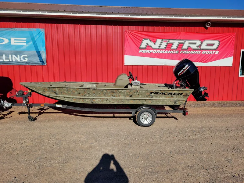 The Image of 2024 Tracker Grizzly 1648 SC fishing boat on trailer, parked outside a red building. - 0