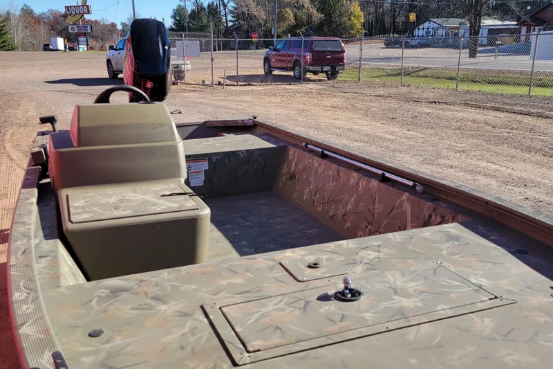 Slide: The Image of 2024 Tracker Grizzly 1648 SC boat with camouflage interior, parked on a dirt lot. - 2