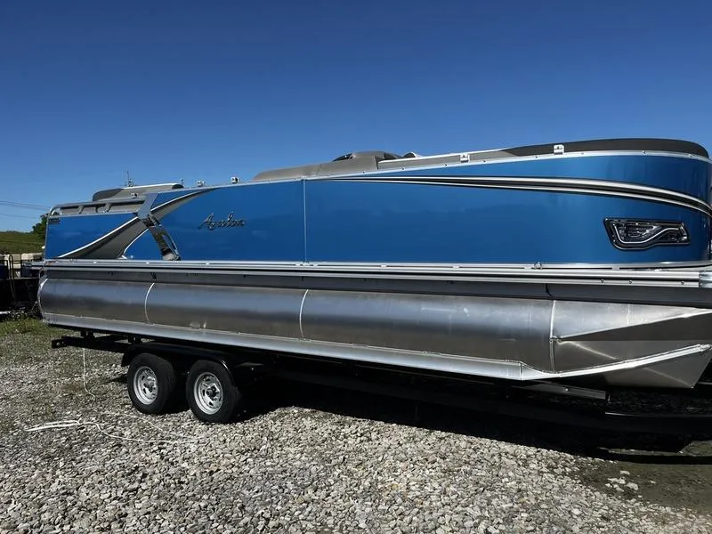 The Image of 2024 Avalon LSZ pontoon boat on a trailer, blue exterior, parked on gravel. - 0