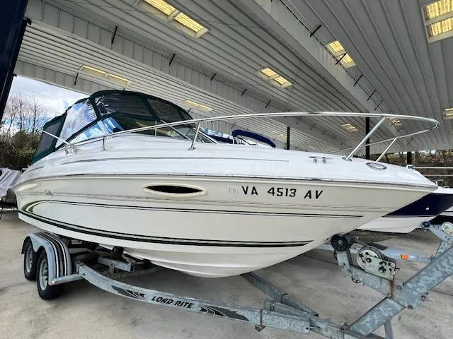 The Image of 1999 Sea Ray 215 Express Cruiser on a trailer in a covered storage area. - 0