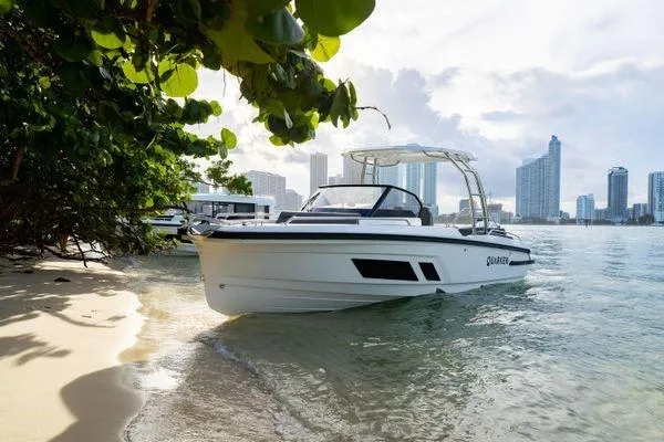 Slide: The Image of 2024 Quarken 27 T-Top V2 boat docked on a sandy beach with city skyline. - 9