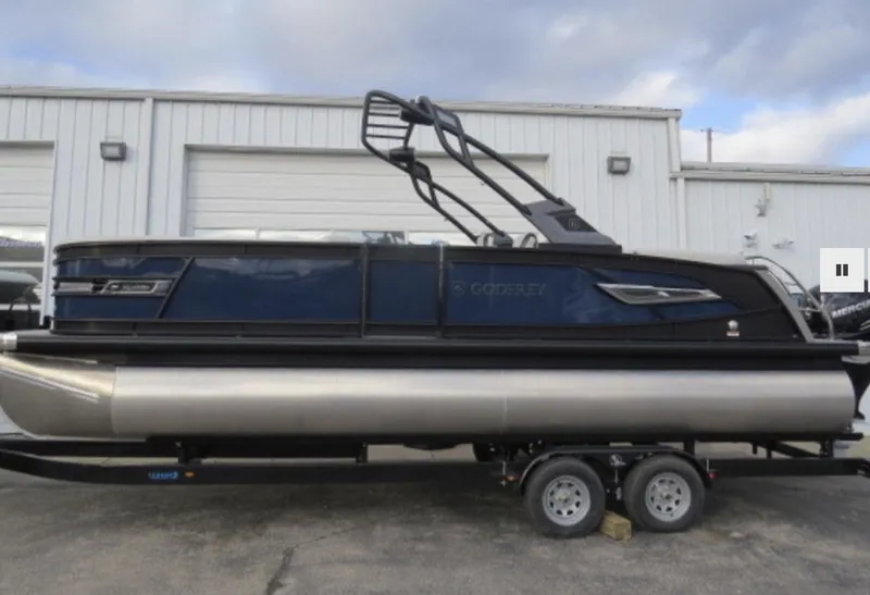 Slide: The Image of 2023 Godfrey AquaPatio 255 SBC pontoon boat on a trailer outside a warehouse. - 1