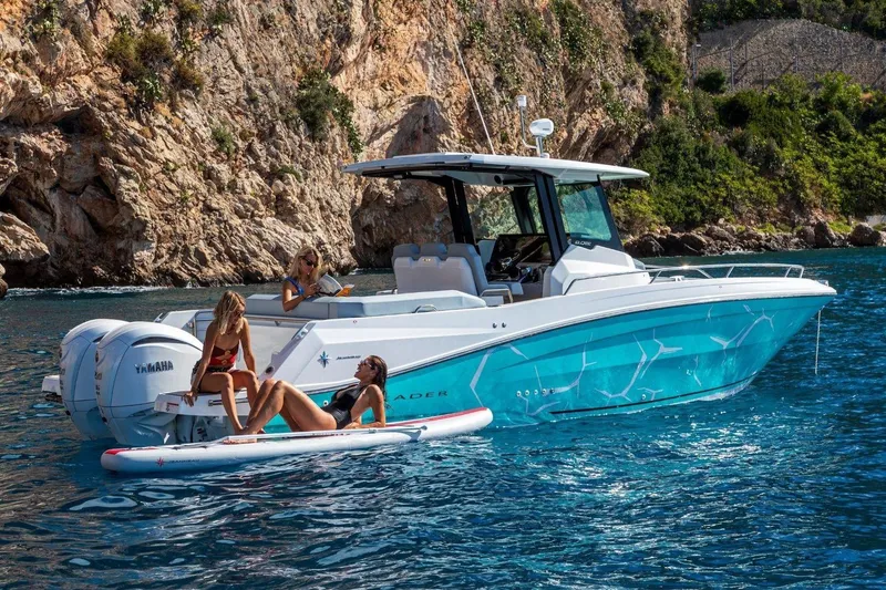 Slide: The Image of 2027 Jeanneau Leader 9.0 CC boat with people relaxing on water, scenic rocky backdrop. - 15
